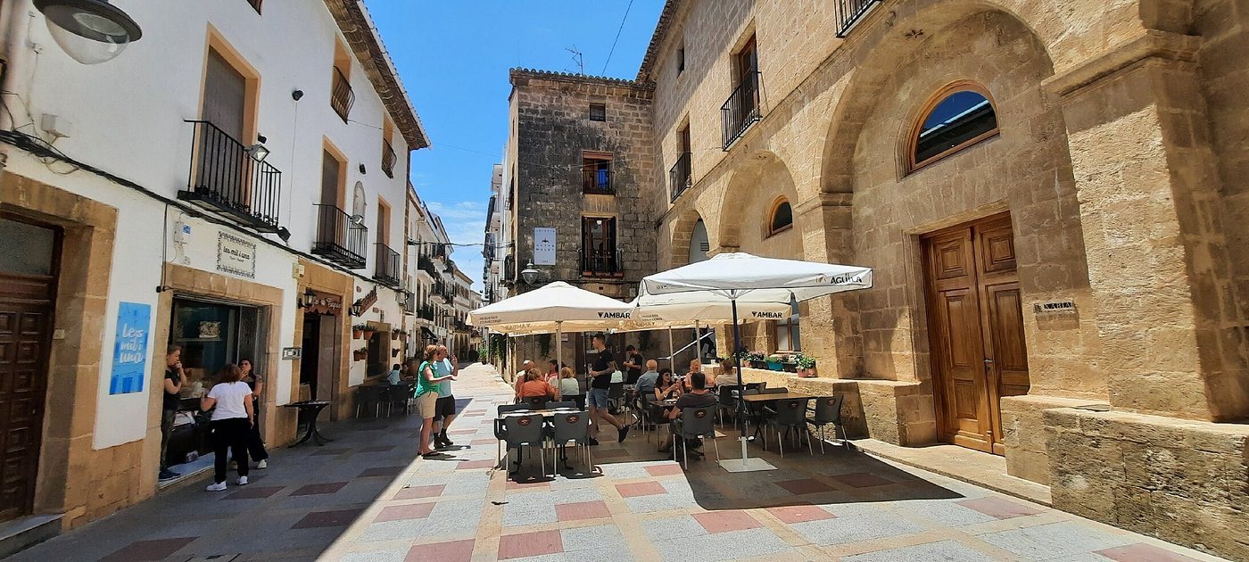 La terrasse du Bar Imperial avec des parasols blancs dans une rue piétonne du centre historique de Jávea, près de façades en pierre