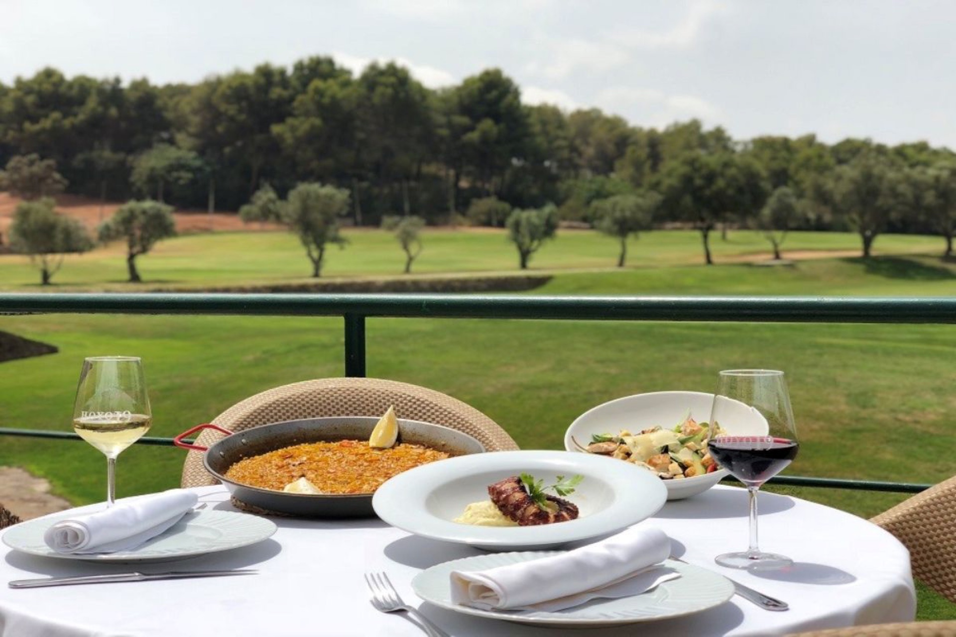 Tisch mit Paella und Wein auf der Terrasse vor dem Golfplatz