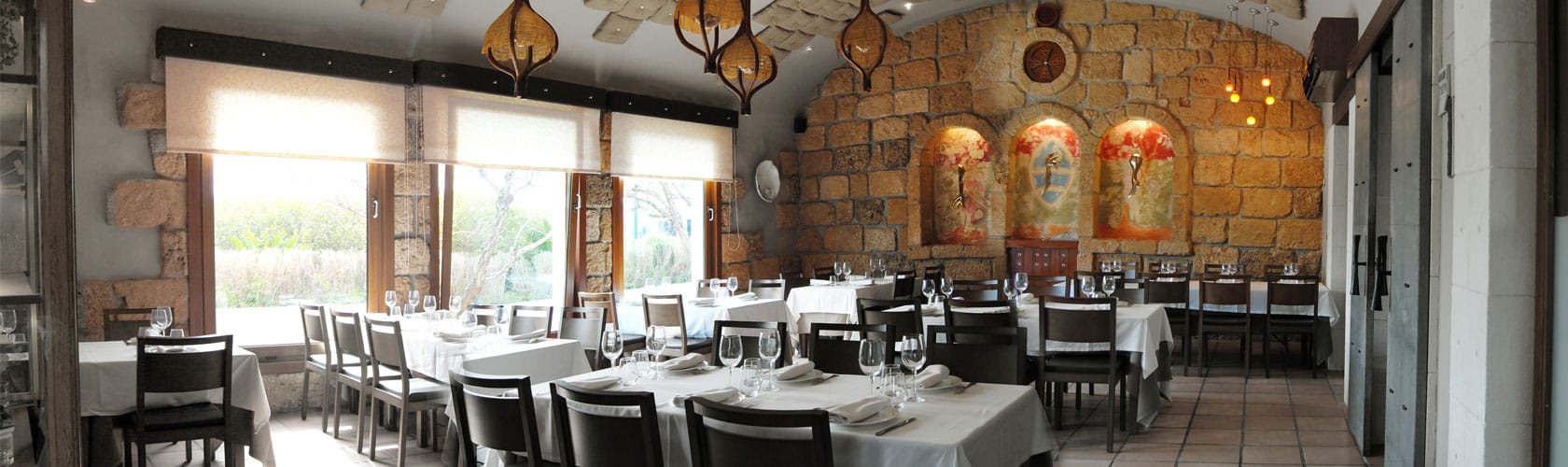 Salle du Restaurante Mezquida avec mur en pierre et grandes baies vitrées