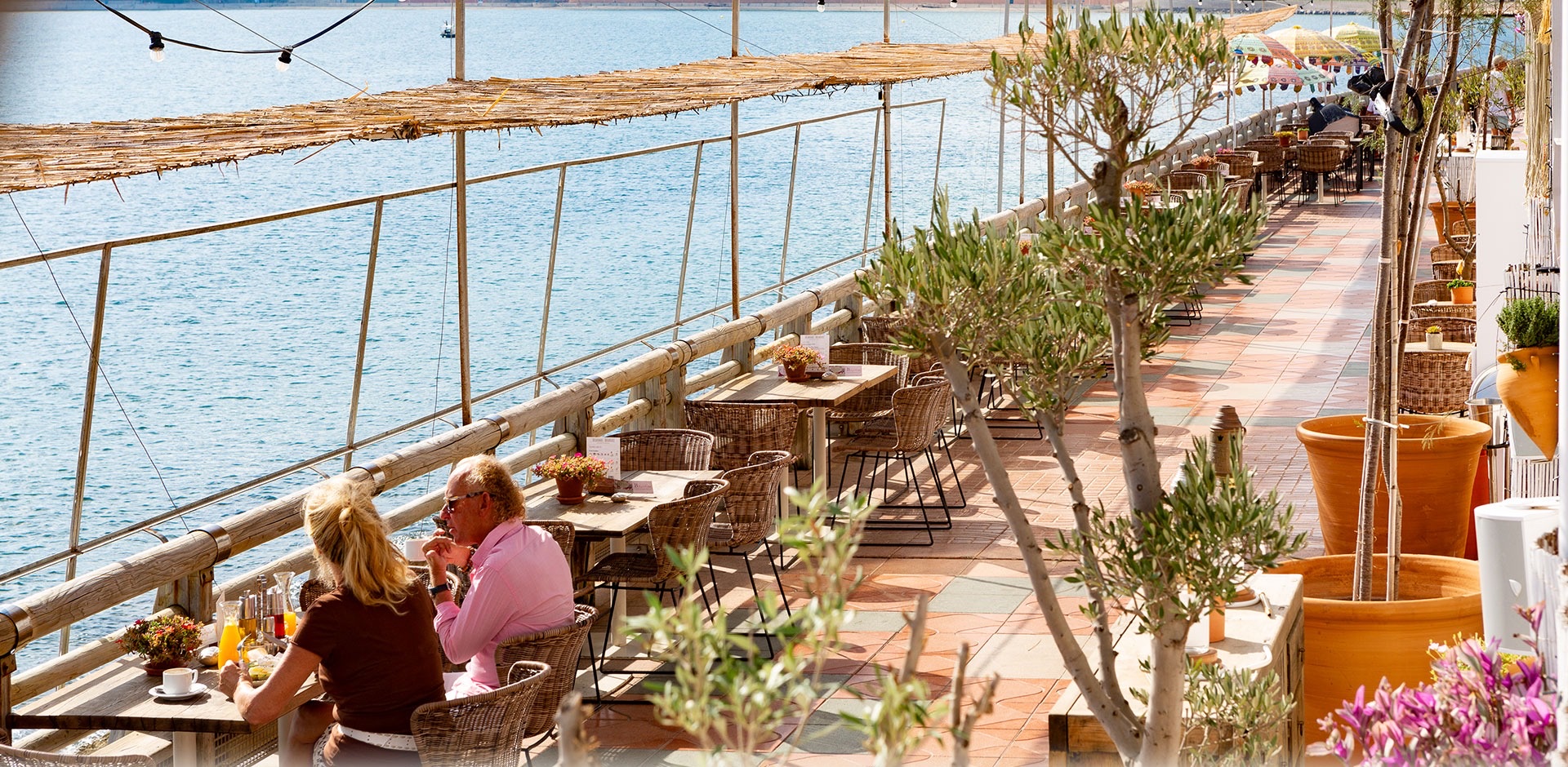 Terrasse en bord de mer, clients prenant le petit-déjeuner sous la canisse